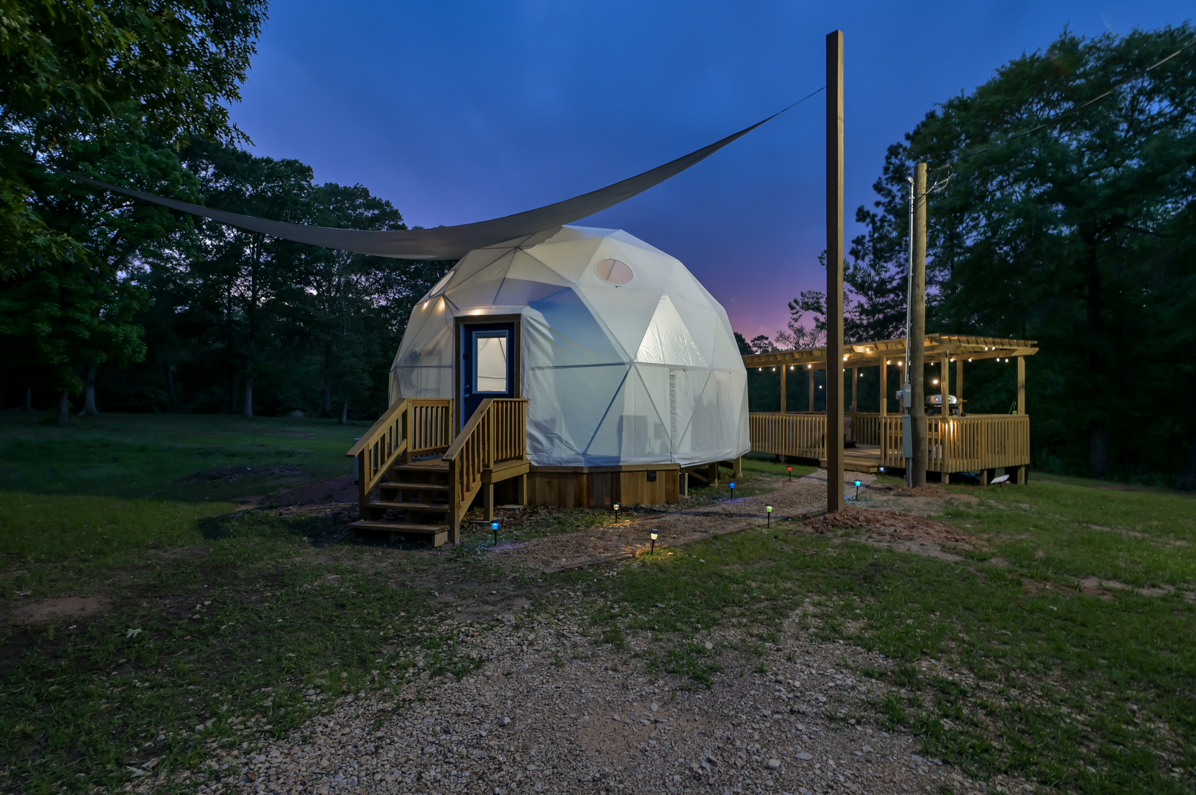 Cameron Ranch Glamping geodesic dome glowing at dusk with string lights and sail shade